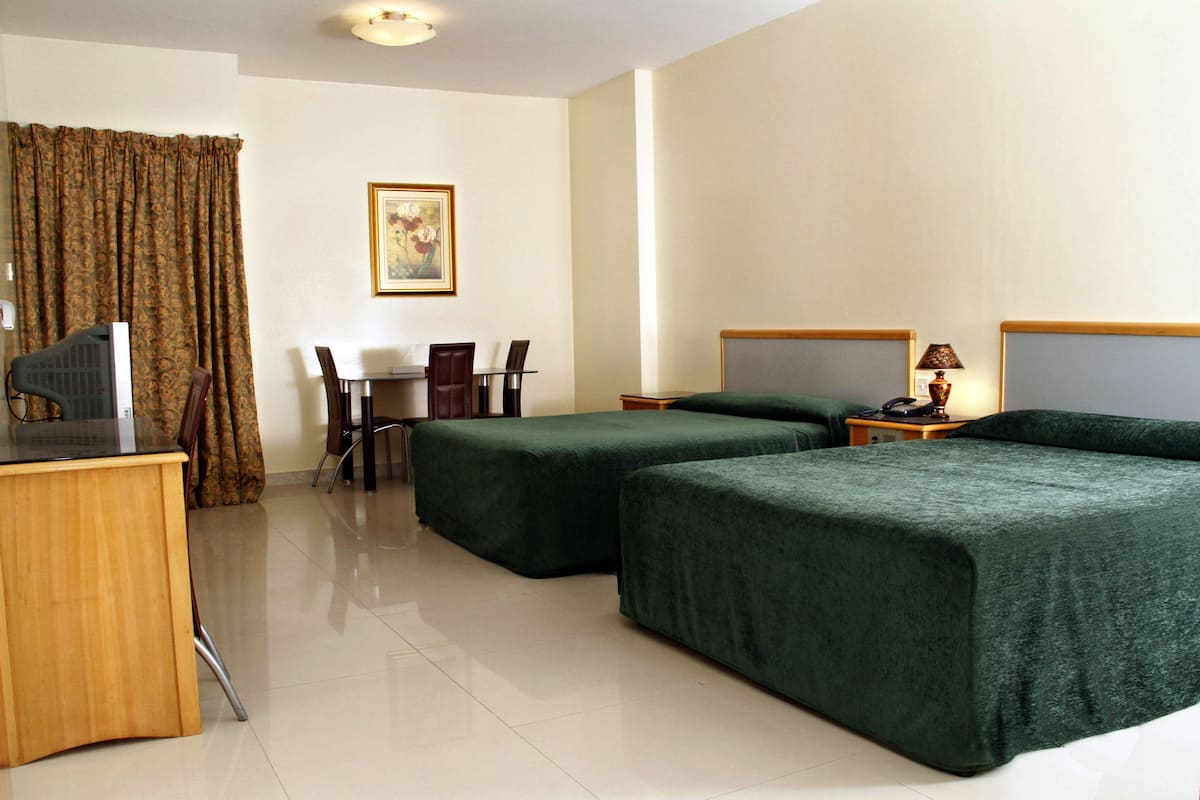 Habitación de hotel con dos camas, un escritorio con computadora, una silla, una lámpara y un cuadro en la pared.