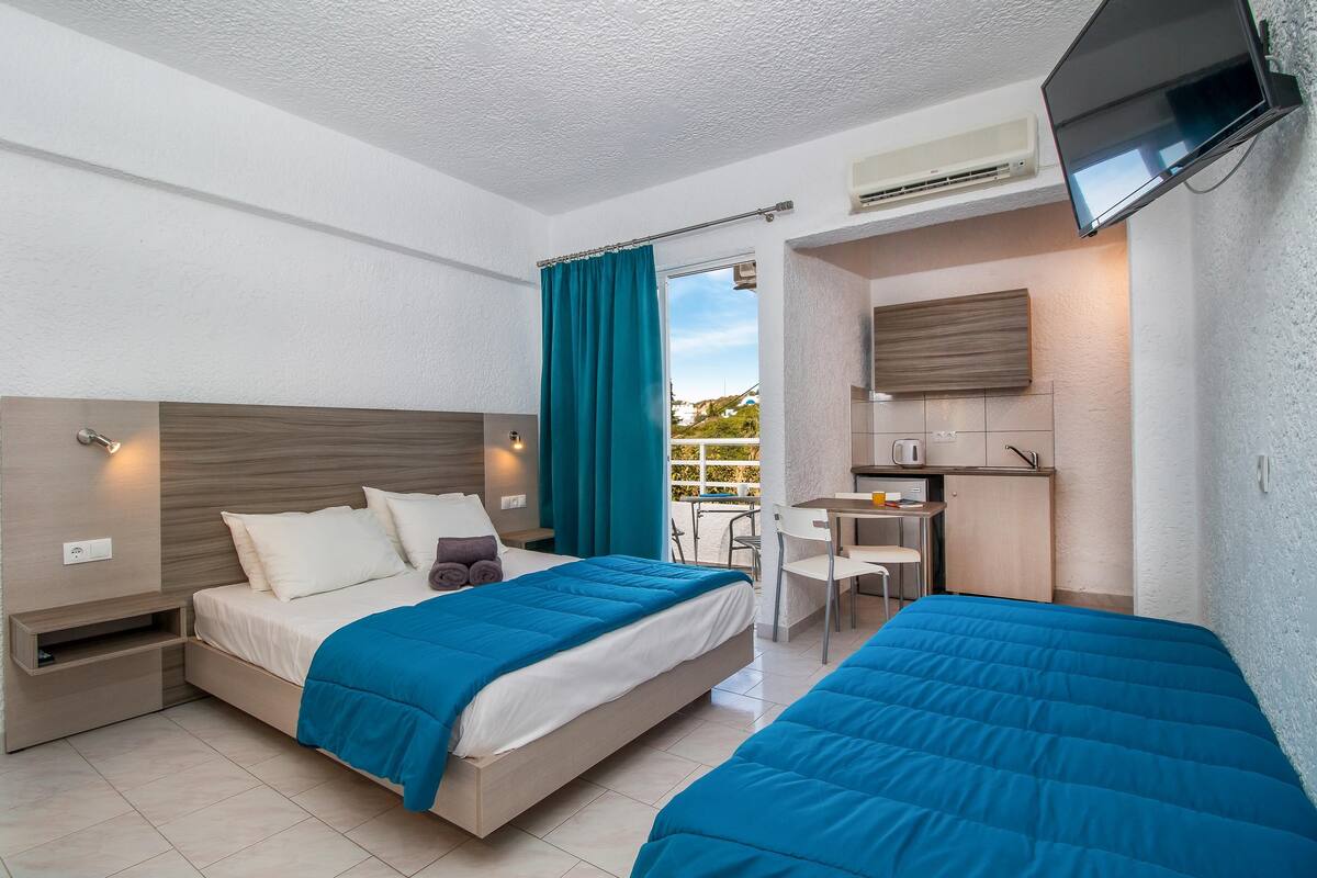 A hotel room with two beds, a kitchenette, and a TV.