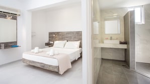 A modern bedroom with a large bed, a wooden headboard, a bedside table, a mirror, and a bathroom with a sink and mirror. - Anika Studios (Rhodes)