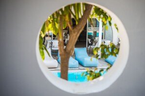 A circular view of a pool area with lounge chairs and a tree, surrounded by a building with a sign reading "Ba. Restcau." - Anika Studios (Rhodes)
