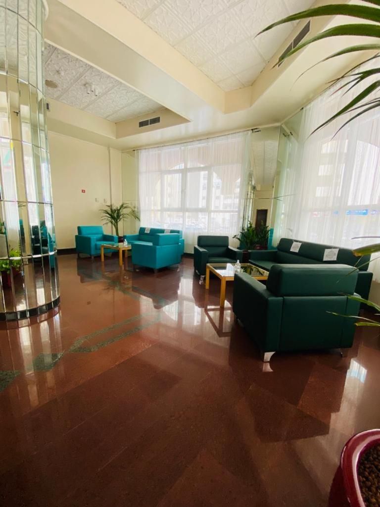 A spacious lobby with a polished wooden floor, teal sofas, and a large mirror reflecting the room.