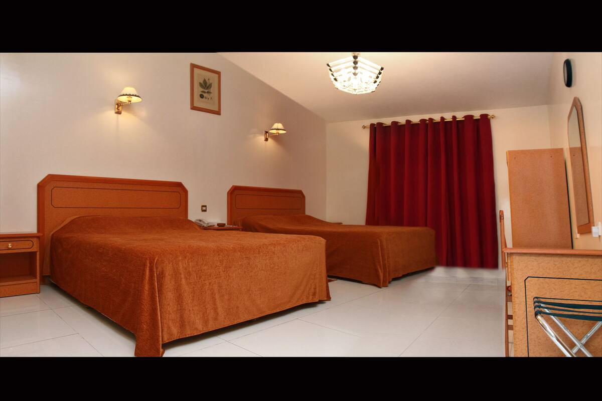 Een hotelkamer met twee bedden, een bureau, een stoel, een spiegel en een rood gordijn.