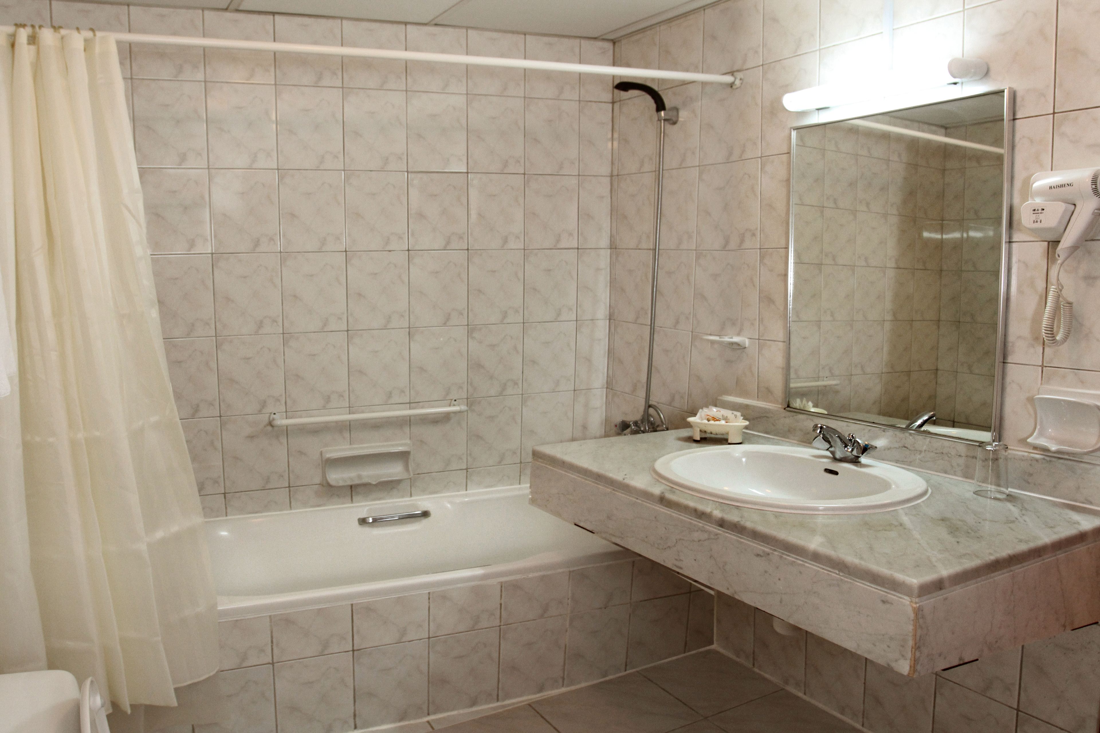 A bathroom with a bathtub, a sink, a mirror, and a hairdryer.