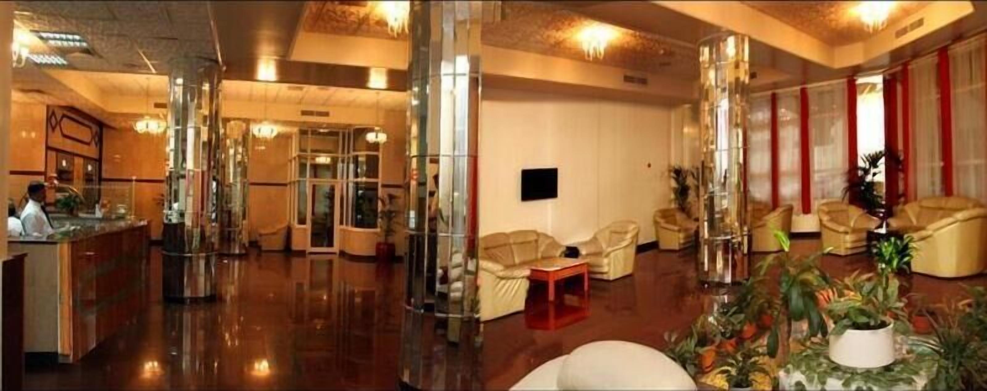 A spacious lobby with a reception desk, a seating area with sofas, and a large potted plant.