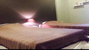 A hotel room with two beds, a nightstand, and a lamp.