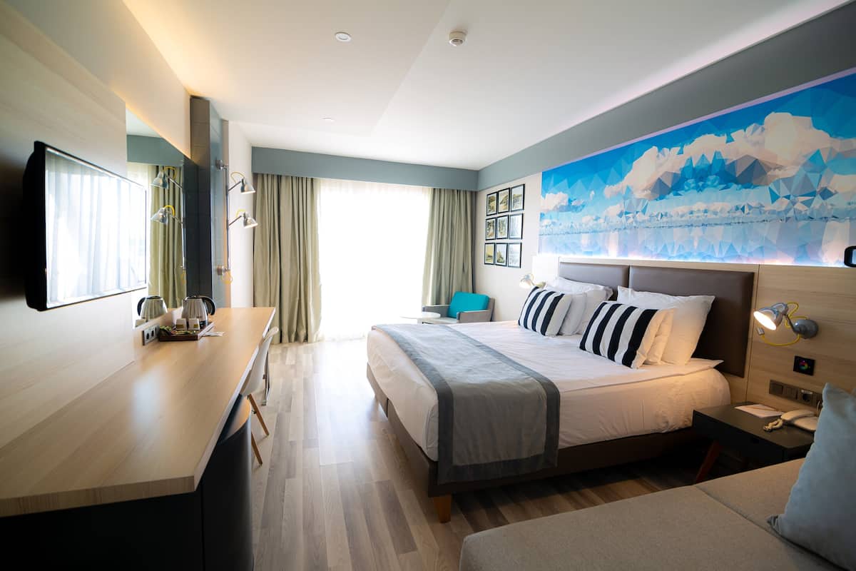 Une chambre d’hôtel moderne, dotée d’un grand lit, d’un bureau et offrant une vue sur l’extérieur.