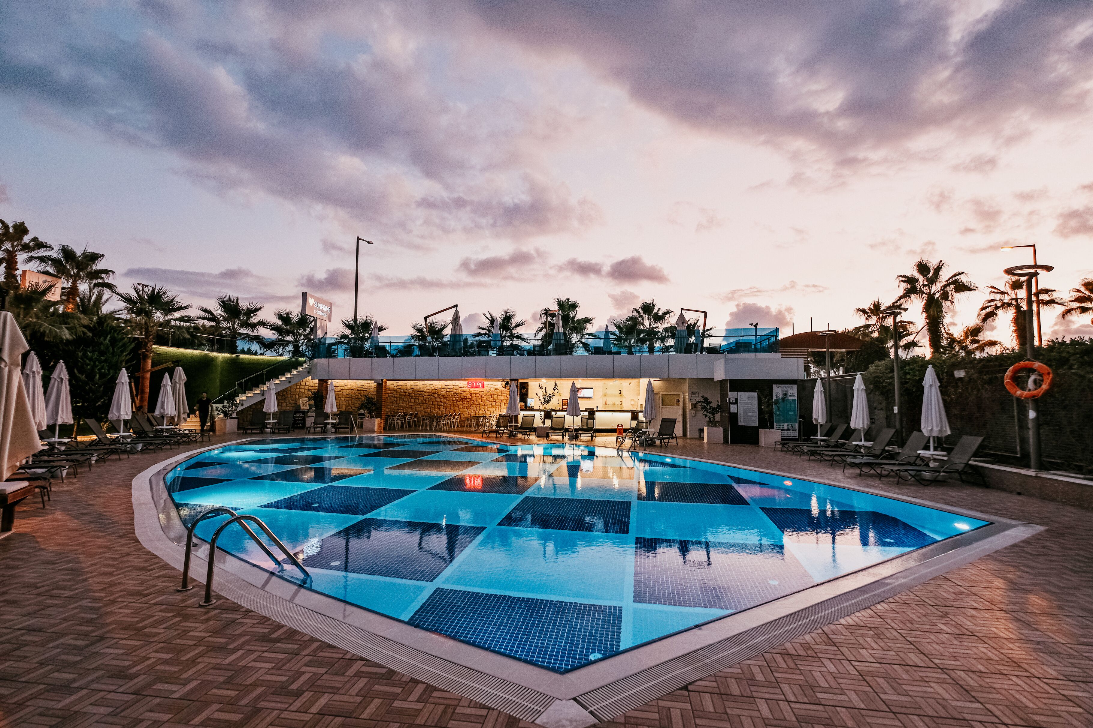 Une piscine avec une terrasse carrelée, des chaises longues et des parasols.
