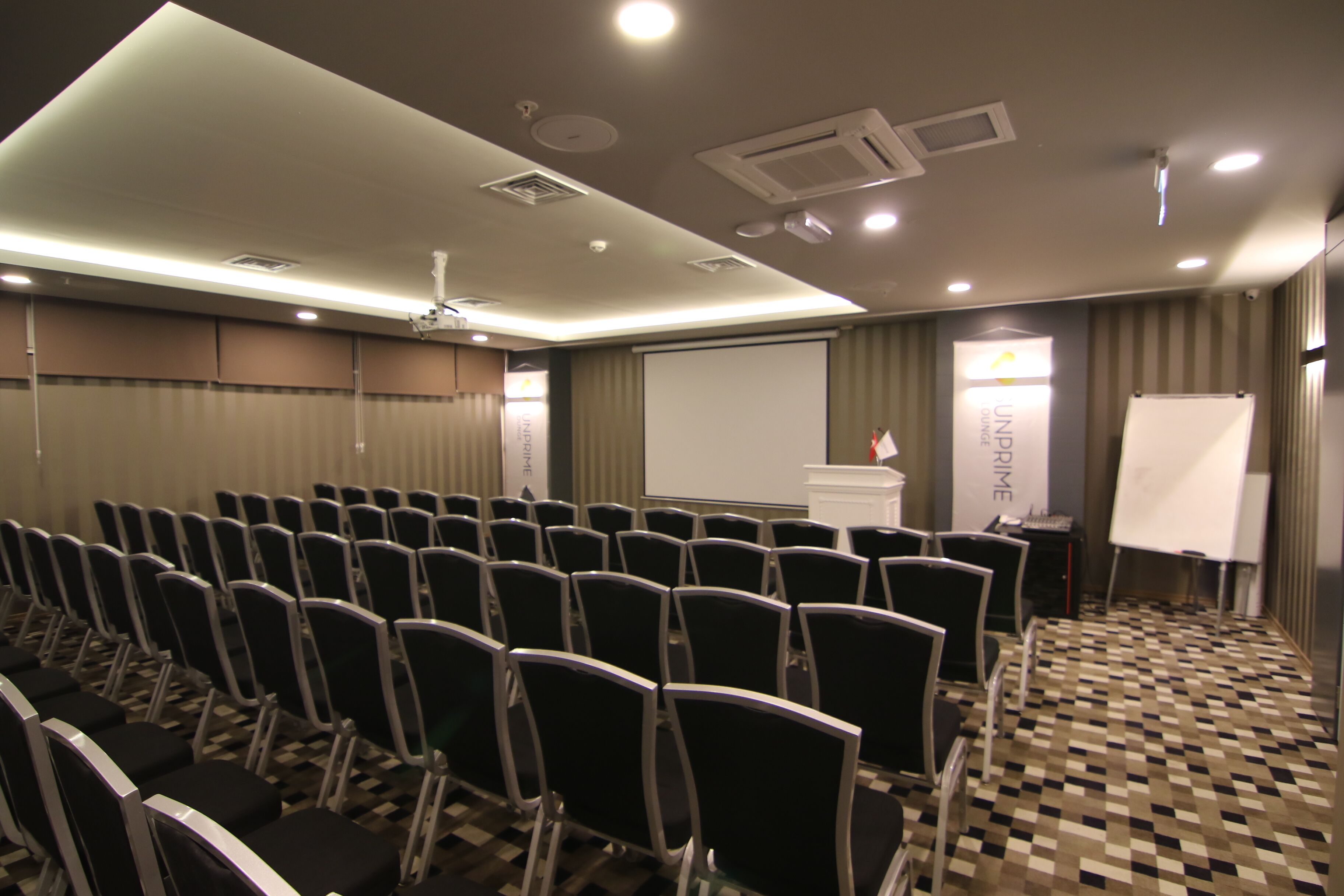 A conference room with rows of chairs, a projector screen, and a whiteboard.