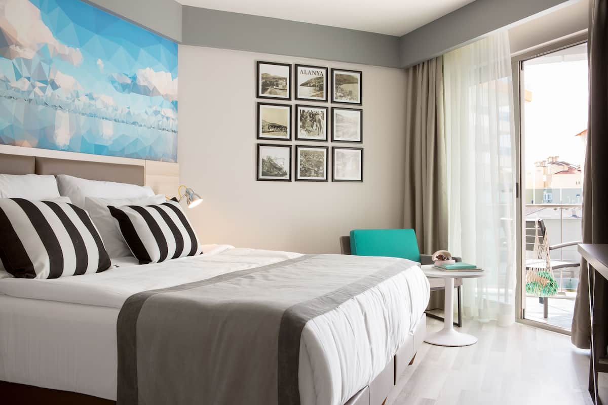 Une chambre d’hôtel moderne avec un grand lit, une petite table, une chaise et un balcon avec vue.