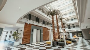 A spacious lobby with a checkered floor, a central seating area, and tall palm trees.