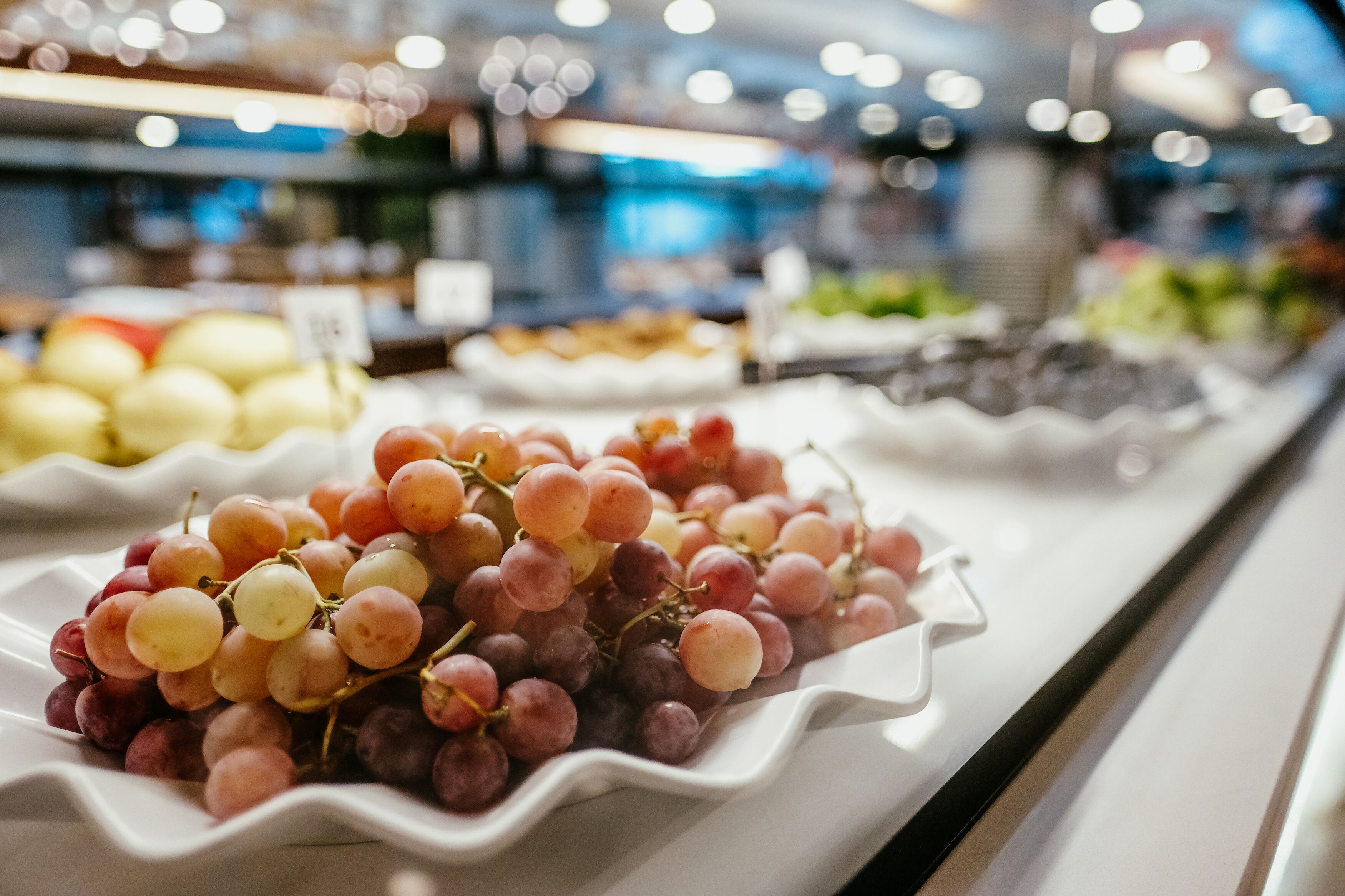 Une étalage de raisins dans un magasin, avec divers fruits en arrière-plan.