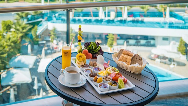 A table with a breakfast spread, including toast, fruit, and a drink, overlooking a pool and ocean view.
