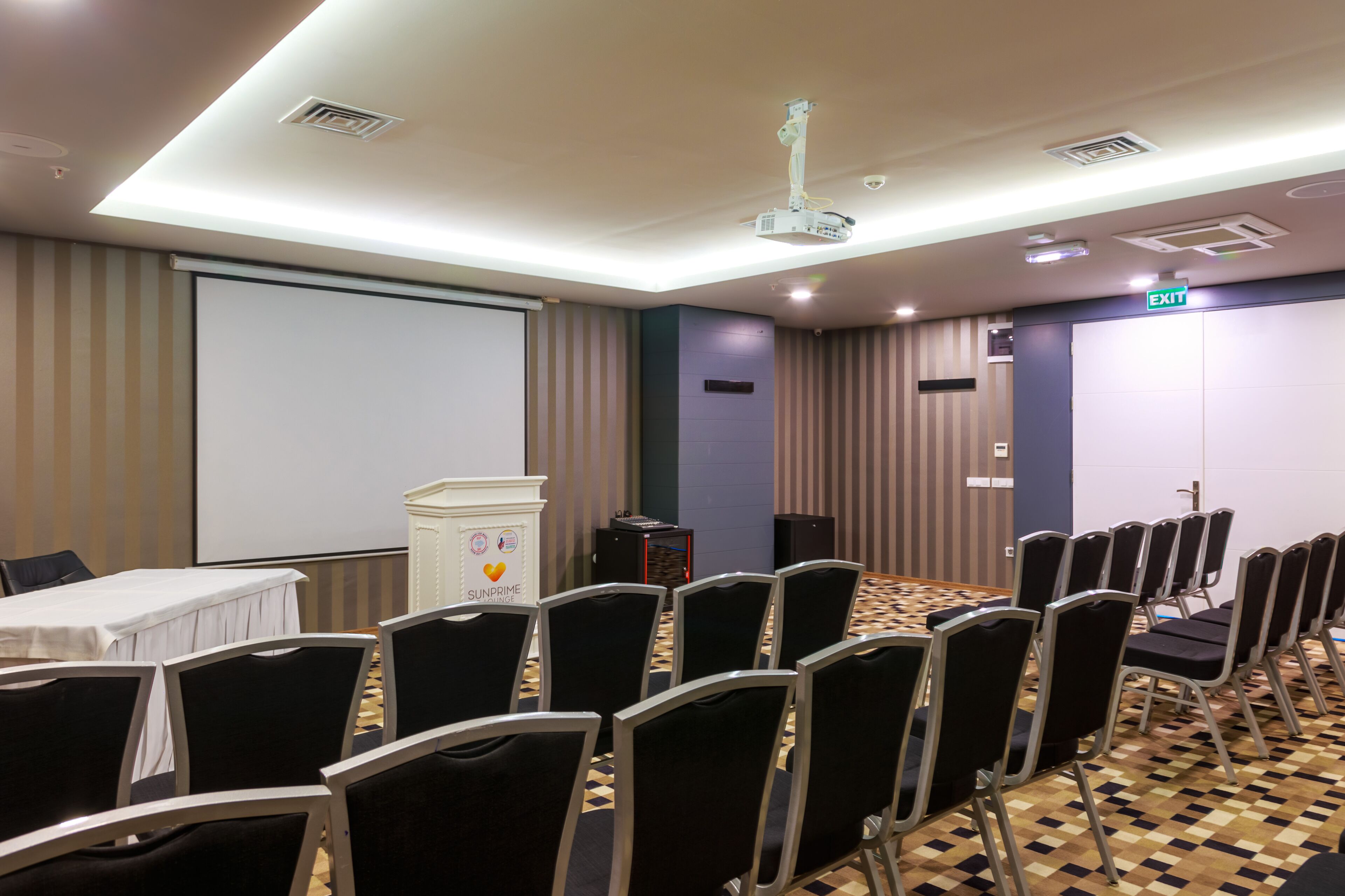 Uma sala de conferências com tela de projeção, um púlpito e fileiras de cadeiras.