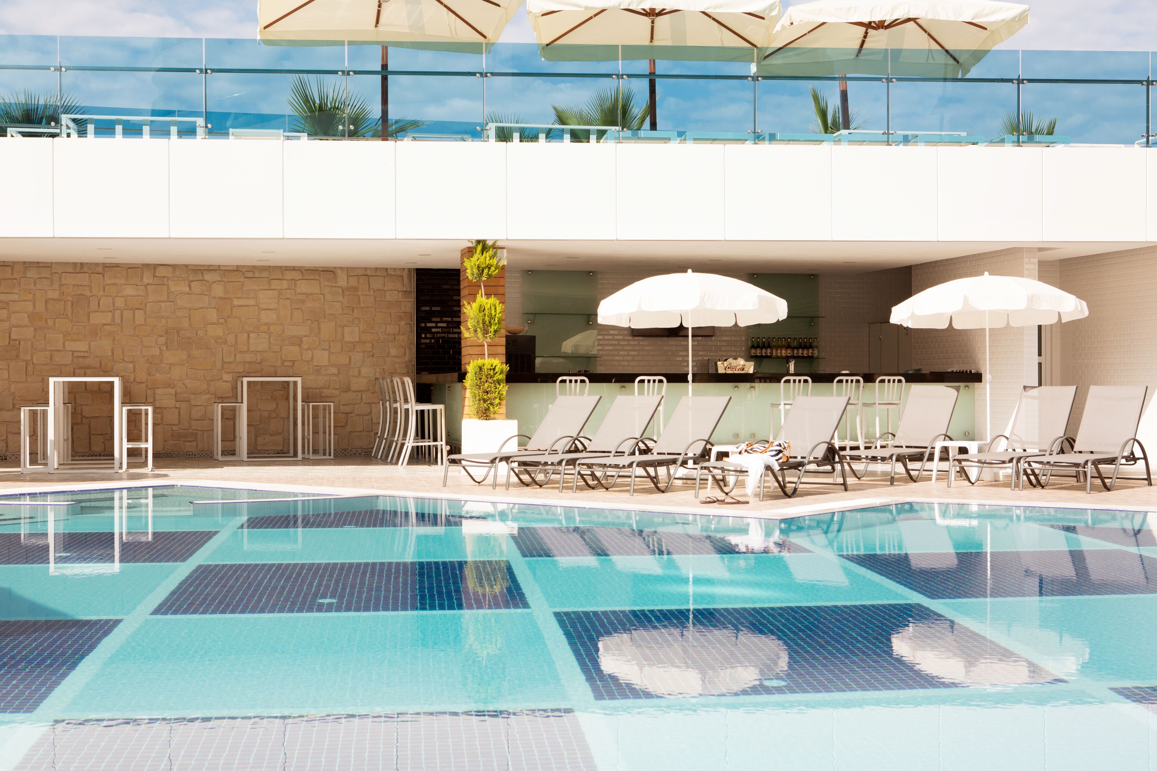 A swimming pool with lounge chairs and umbrellas, a bar area, and a view of the ocean.