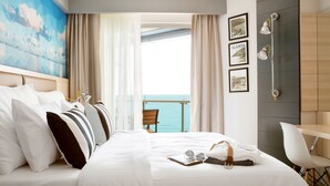 A hotel room with a bed, a desk, and a view of the sea.