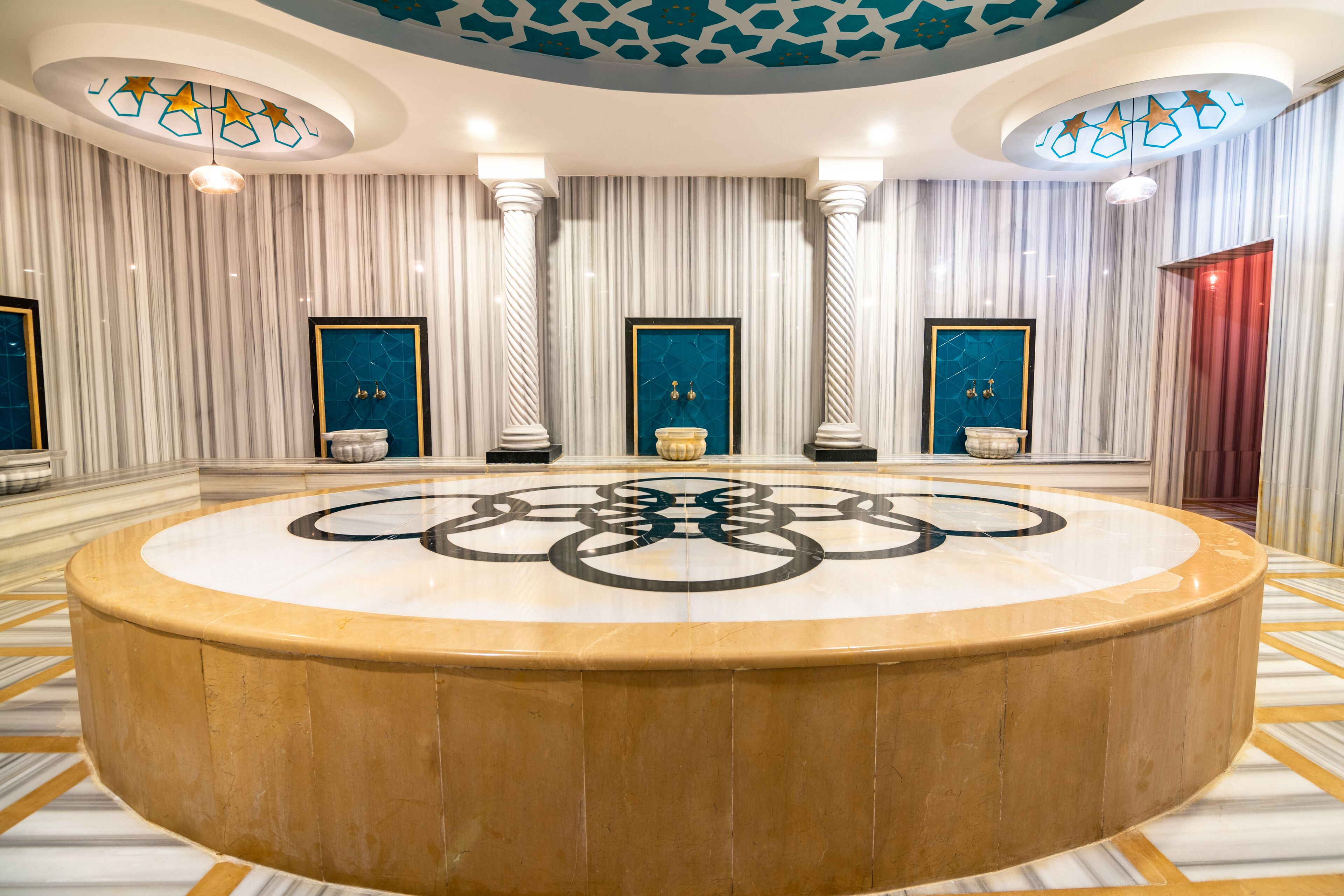 Un vestíbulo espacioso con una mesa circular de mármol en el centro, altas columnas y un techo con diseño.