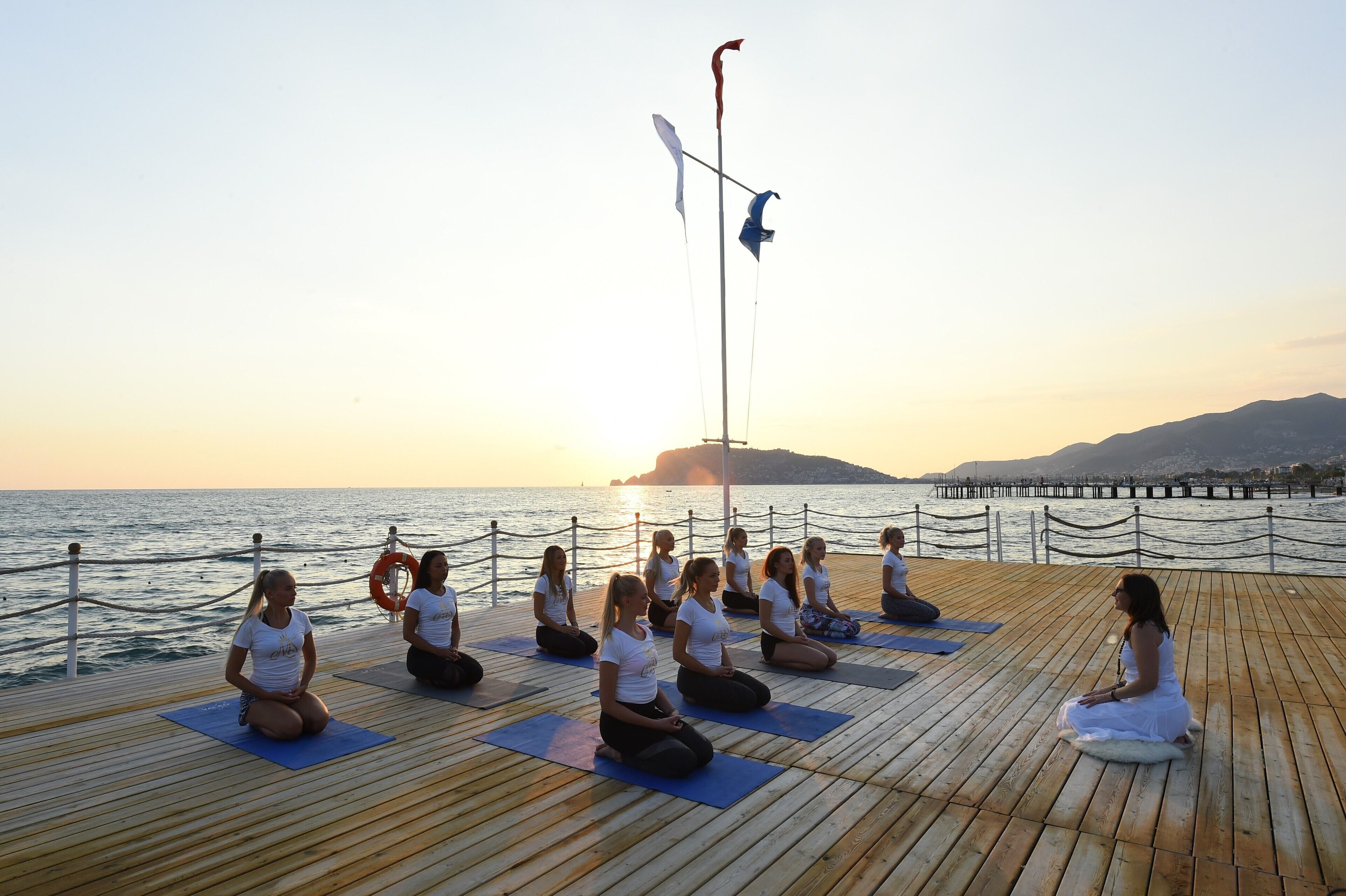 Un grupo de personas meditando en una cubierta de madera junto al agua durante el atardecer.