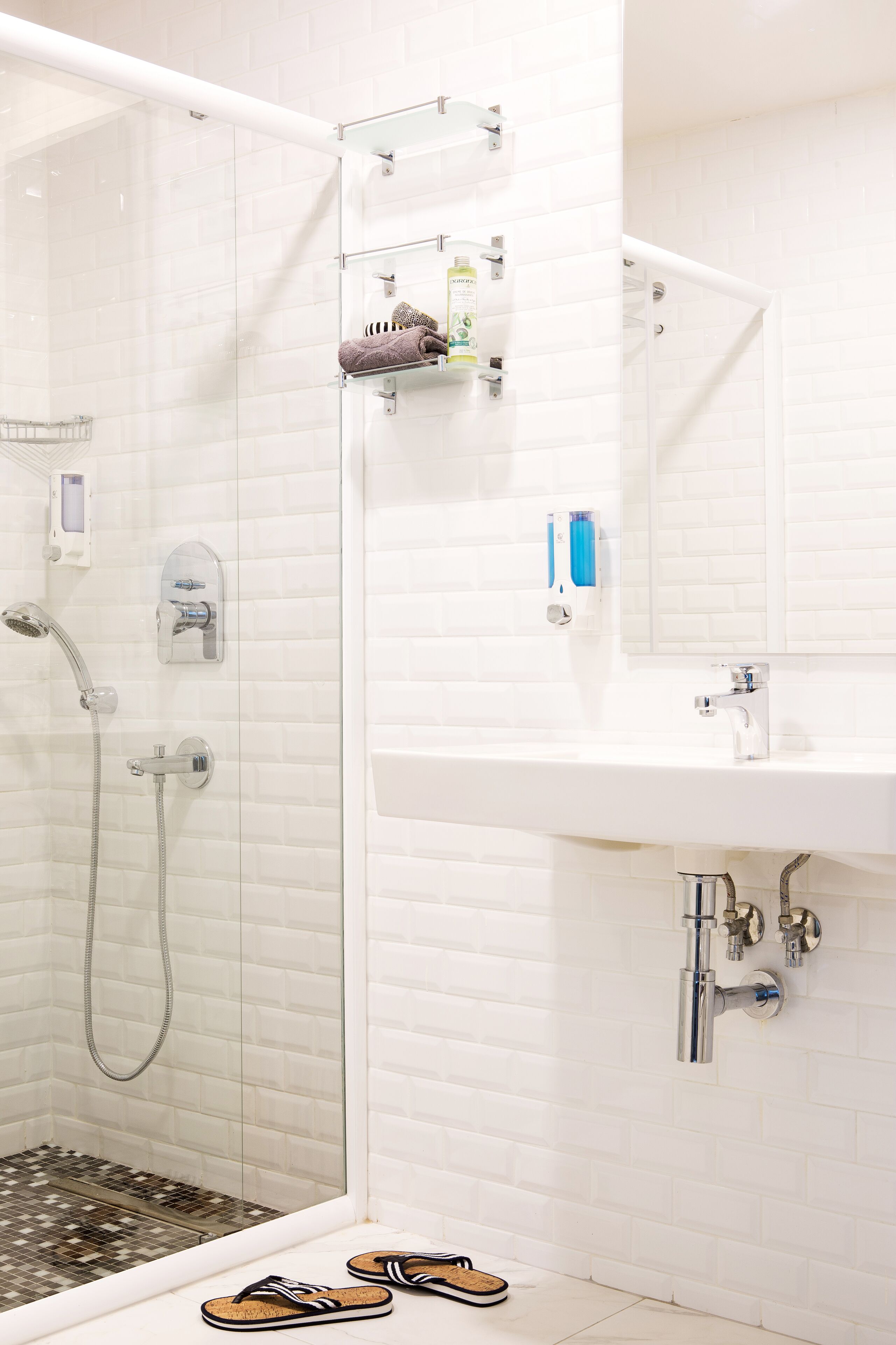 Un baño con ducha envuelta en vidrio, un lavabo blanco y un espejo.