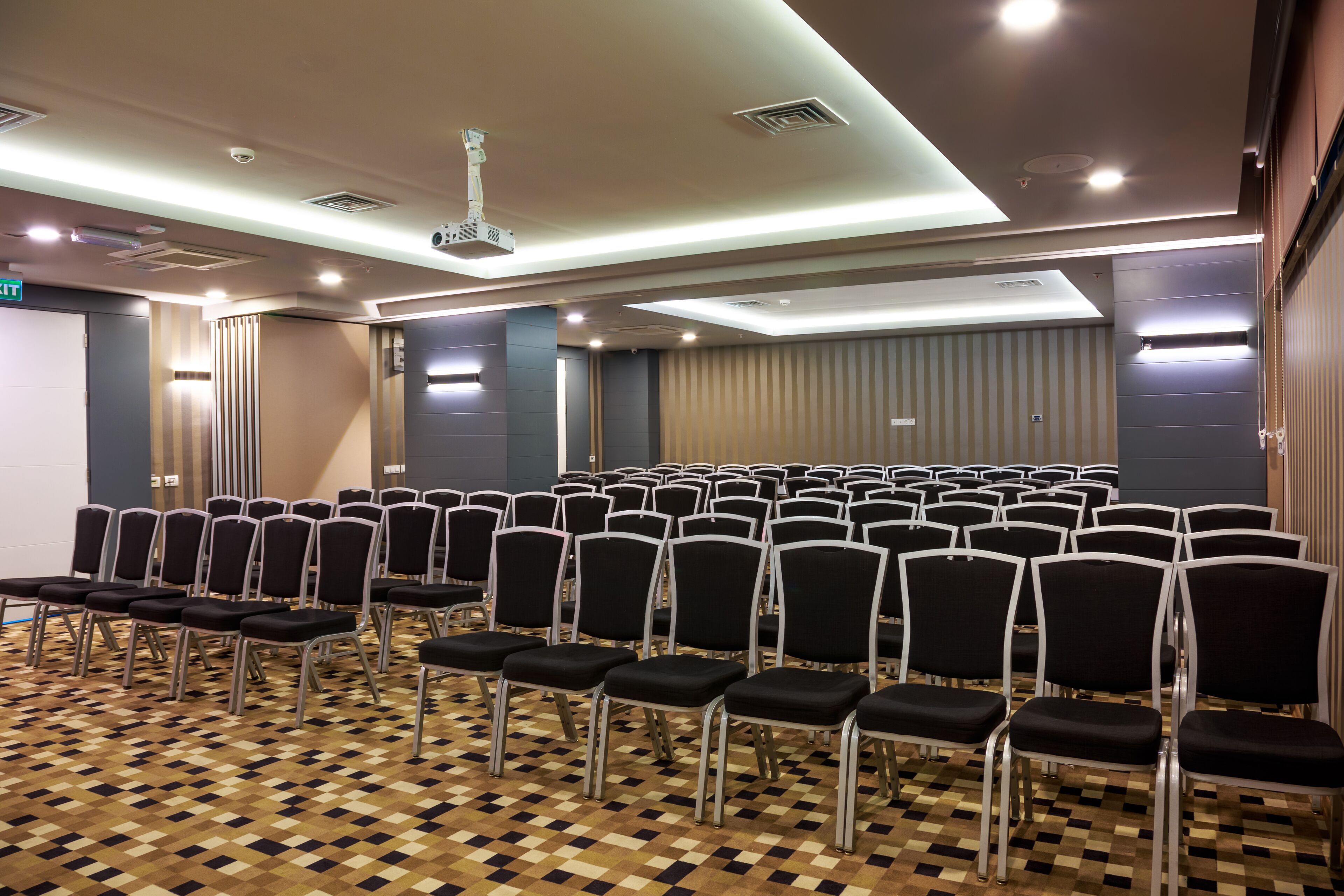 Un salón de conferencias con hileras de sillas negras, piso estampado e iluminación empotrada.