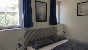 Un dormitorio con cama, mesita de noche, lámpara y ventana con cortinas.