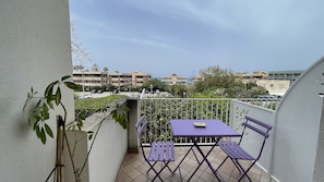 A balcony with a purple table and chairs, a potted plant, and a view of buildings and cars in the background. - Lumachella B&B (Cefalù)
