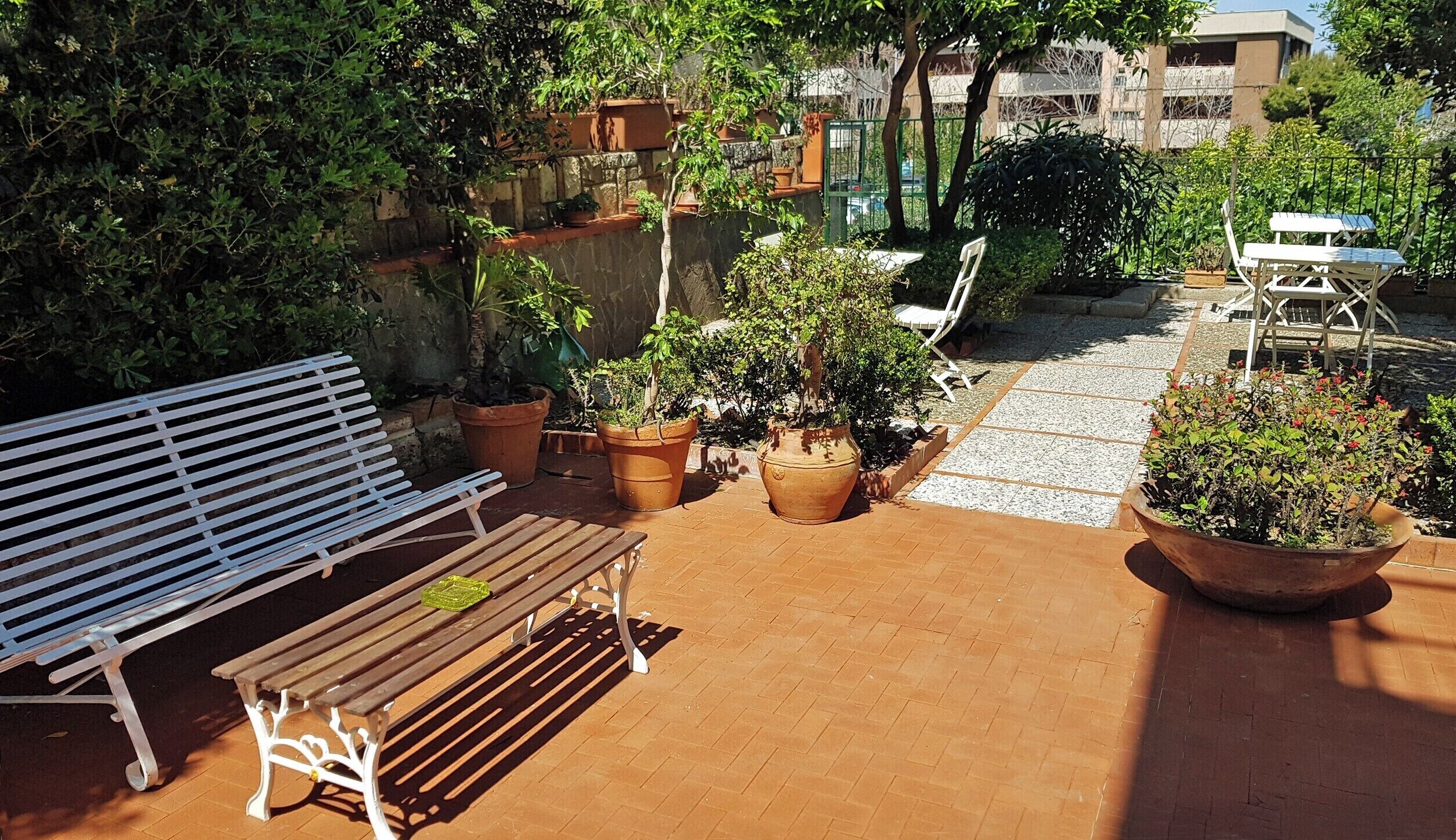 Une terrasse avec un banc en bois, des plantes en pot et une table et des chaises blanches.
