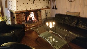 A cozy living room with a brick fireplace, a glass coffee table, leather sofa, and a wooden ceiling. - Kvarngården Natur Resort (Byxelkrok)