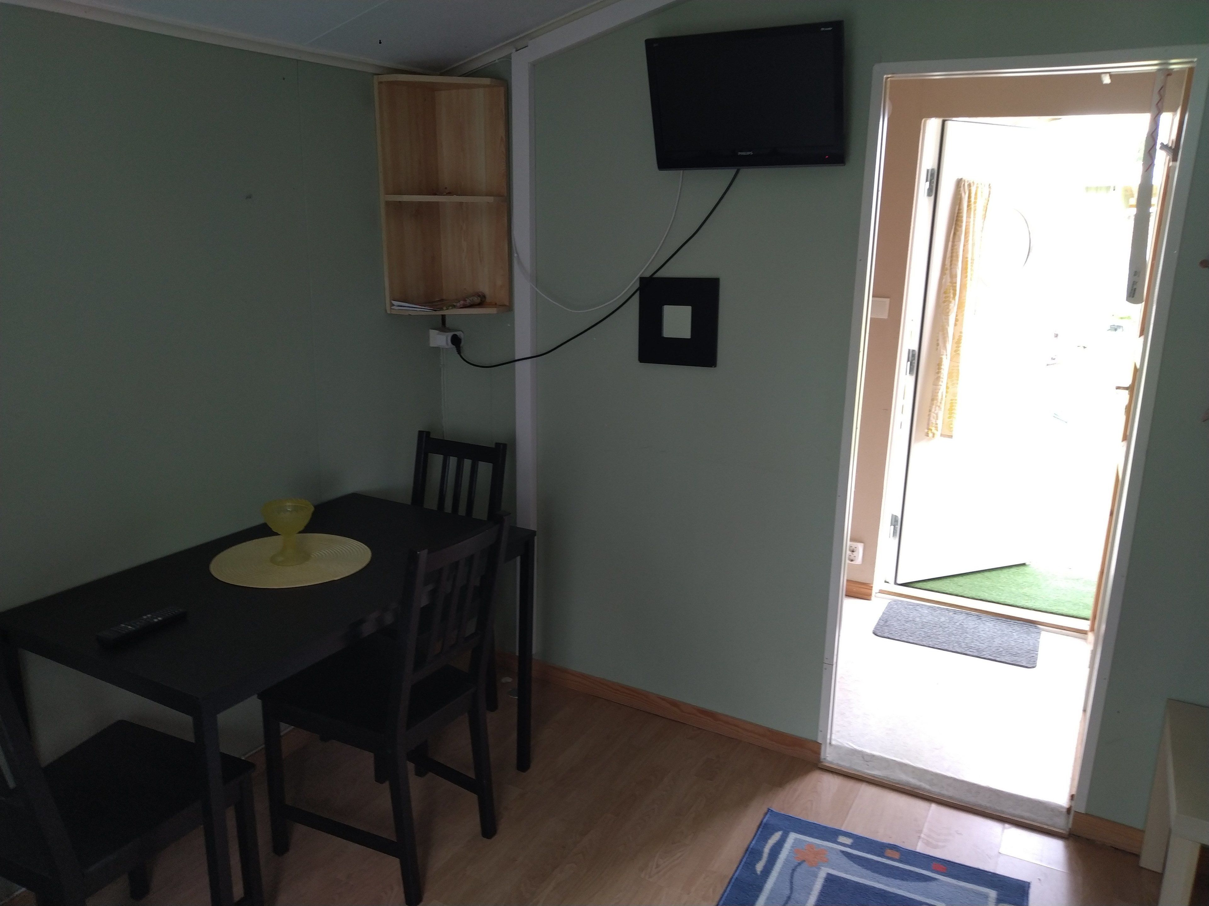 Un comedor con una mesa, sillas, un televisor montado en la pared y una puerta que da al exterior.