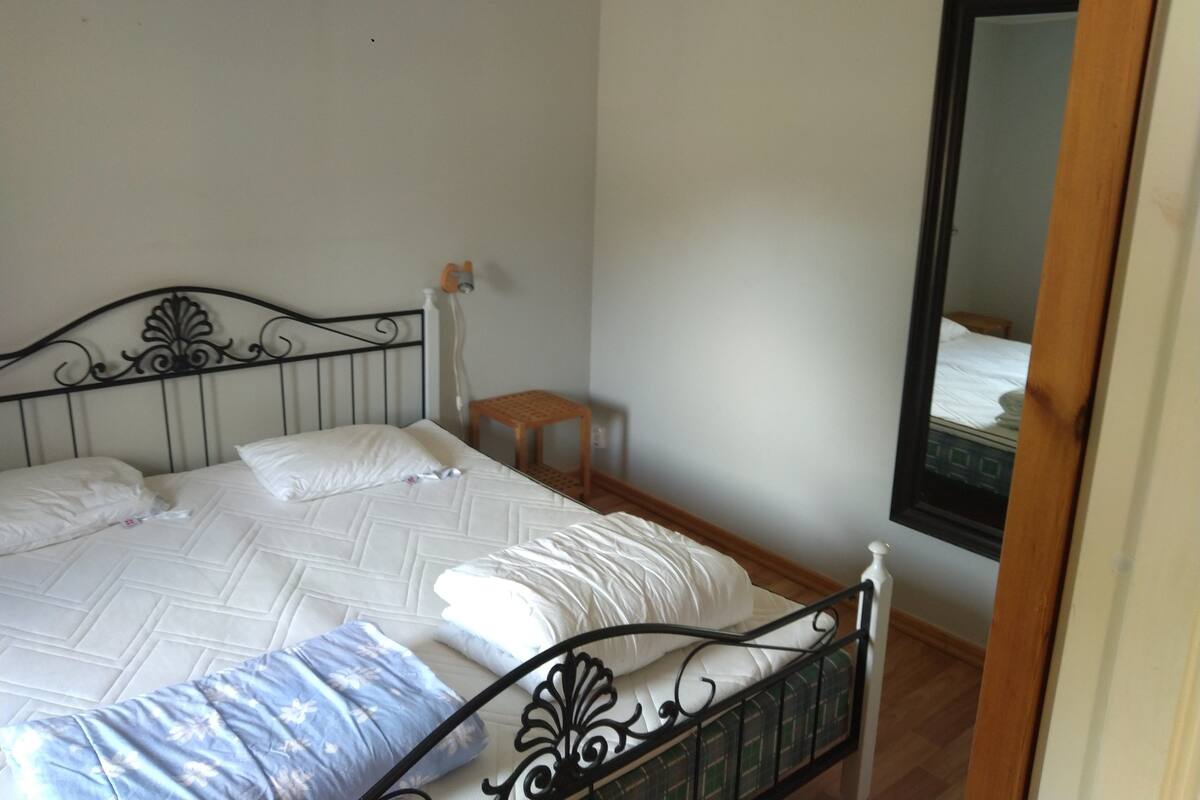 Un dormitorio con cama, un taburete de madera y un espejo en la pared.