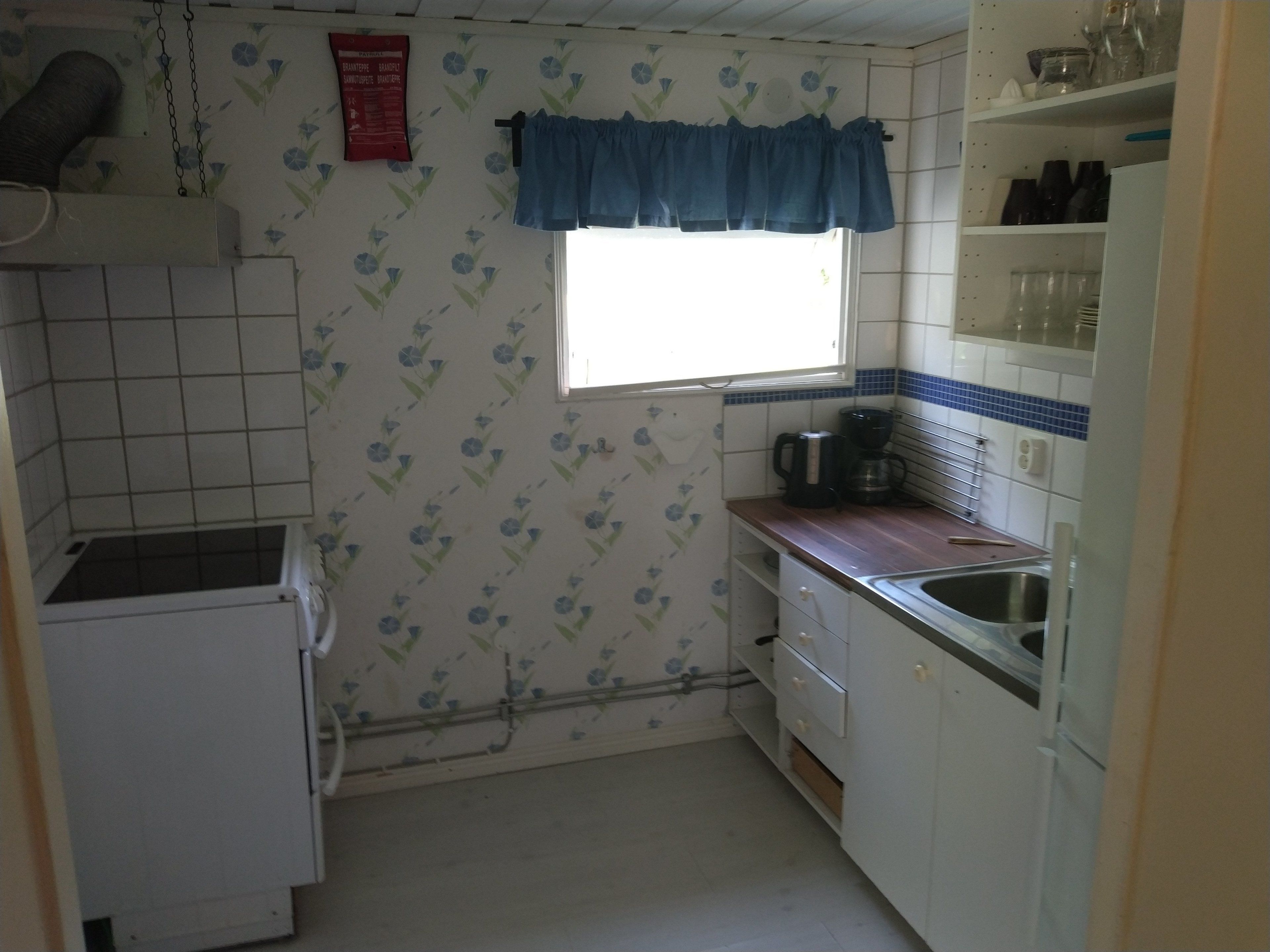 A small kitchen with a window, white cabinets, a sink, and a coffee maker.