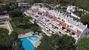 Un complejo residencial moderno con varias edificaciones de dos pisos, una piscina central y zonas verdes circundantes.