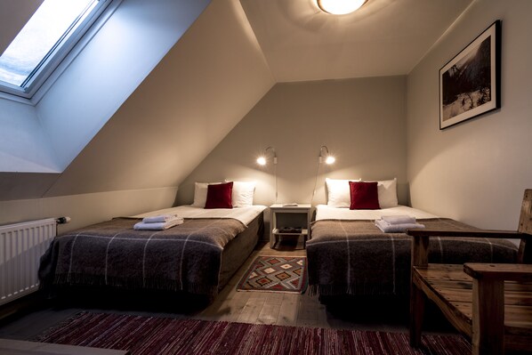 A small, cozy room with two beds, a wooden chair, a small table, and a skylight.