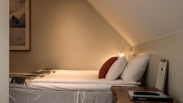 Un dormitorio con una cama, almohadas, una lámpara de noche, una mesita de noche de madera y un cuadro en la pared.