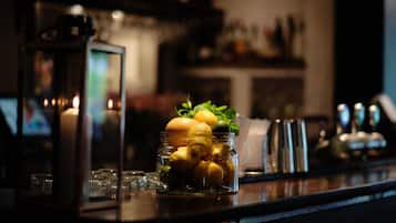 A glass jar filled with lemons and oranges on a bar counter, with a candle and a lantern in the background.