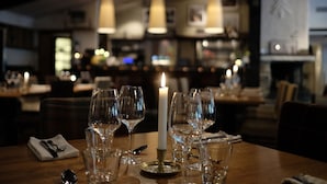 A dining table set with wine glasses, a candle, and cutlery, with a bar and ambient lighting in the background. - Granen Hotell & Restaurang (Are)