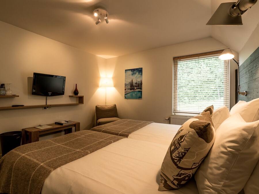 Une chambre d’hôtel avec deux lits, une télévision, un bureau et une fenêtre avec des stores.