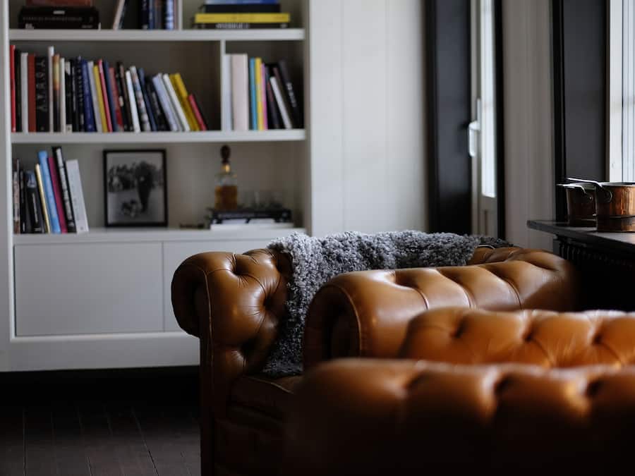 A brown leather sofa in a room with a bookshelf filled with books and a framed picture.