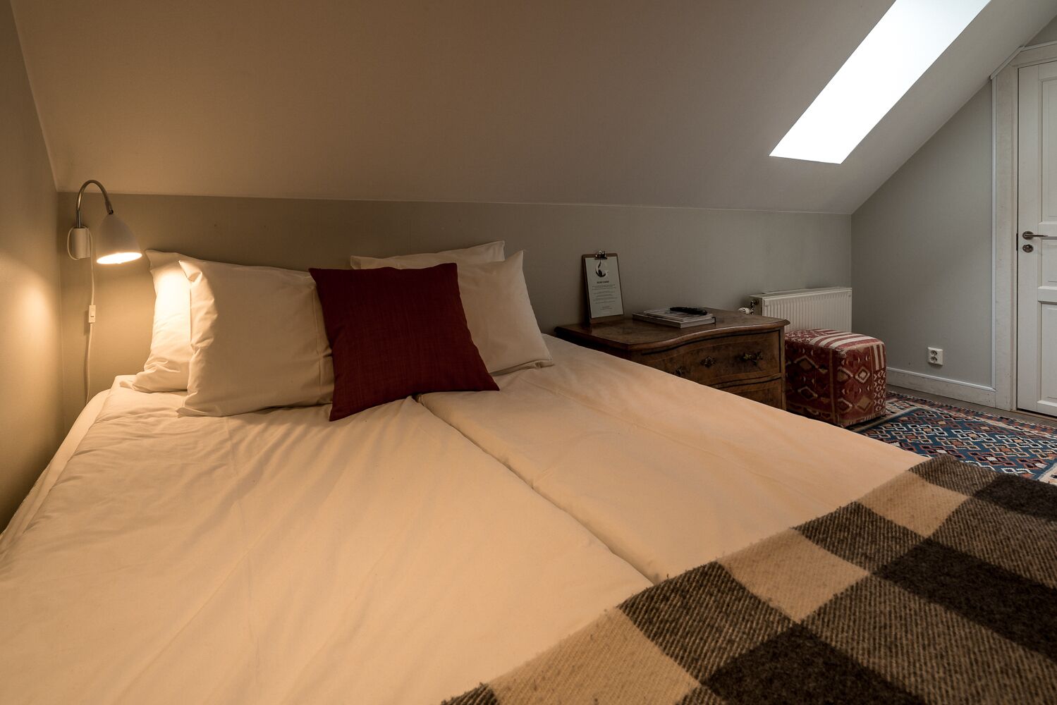 Un dormitorio con cama, mesita de noche, cómoda, alfombra estampada y tragaluz.