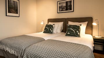 Quarto bem arrumado com uma cama grande, duas almofadas com estampa de mapa, um cobertor estampado e duas fotos emolduradas na parede.