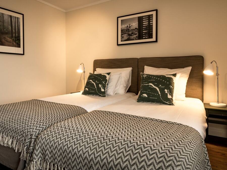 Quarto bem arrumado com uma cama grande, duas almofadas com estampa de mapa, um cobertor estampado e duas fotos emolduradas na parede.