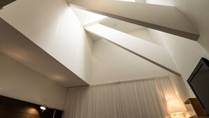 A room with a sloped ceiling, a window with curtains, and a lamp on the side. - Granen Hotell & Restaurang (Are)