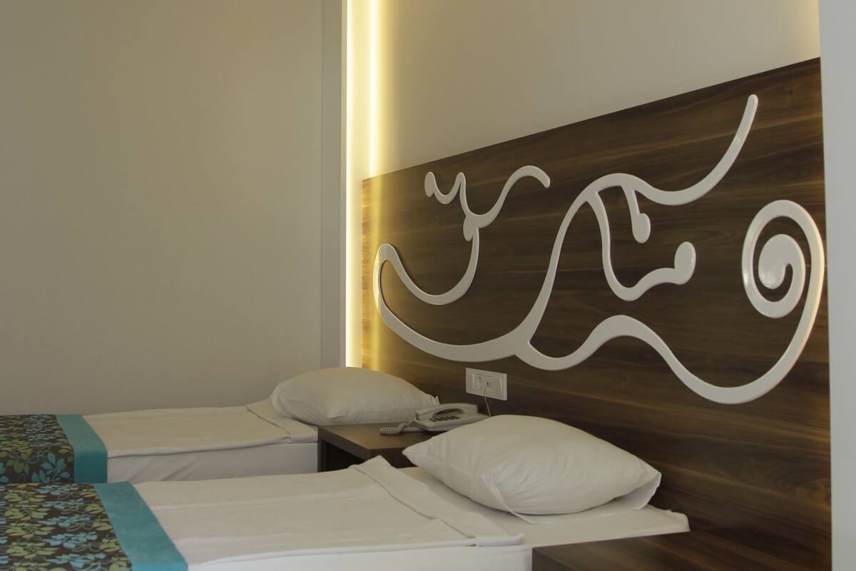 Ein Hotelzimmer mit zwei Betten, einem Holzkopfstück und einem an der Wand hängenden Kunstwerk.