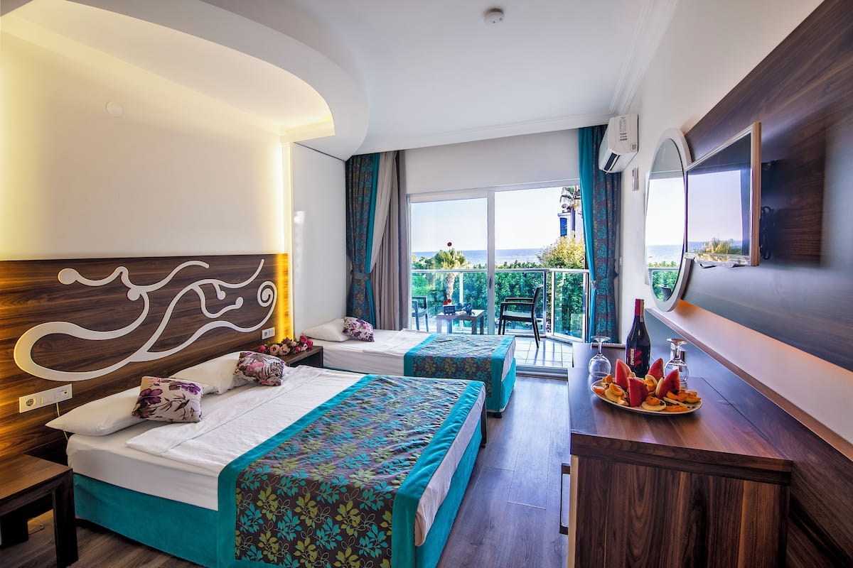Ein Hotelzimmer mit zwei Betten, einem Balkon mit Blick, einem Essbereich und einem Obstteller sowie einem Fernseher an der Wand.