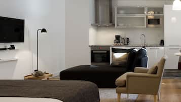 Ett modernt och kompakt bostadsutrymme med en säng, en soffa, en TV, ett litet kök och en matplats.