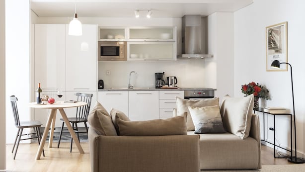 Une cuisine moderne avec des armoires blanches, une hotte en acier inoxydable et un coin repas comprenant une table et des chaises.