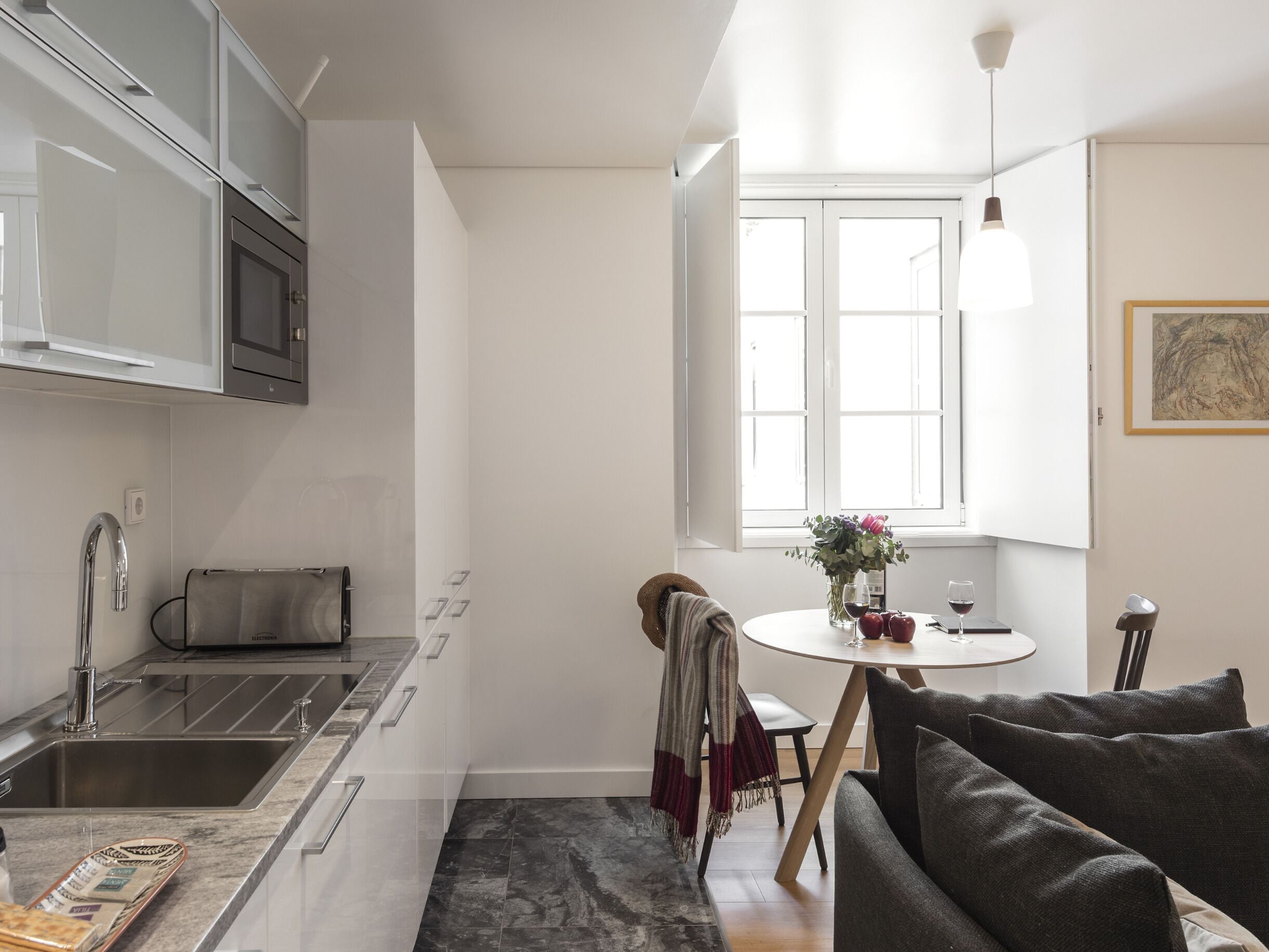 A modern kitchen with a built-in oven, a dining area with a round table, and a window with natural light.