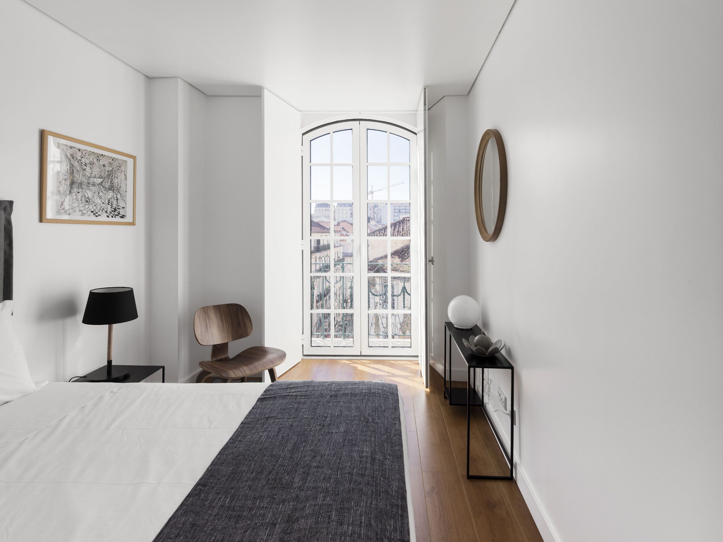 A modern bedroom with a large bed, a chair, a desk, a lamp, and a view through a glass door.