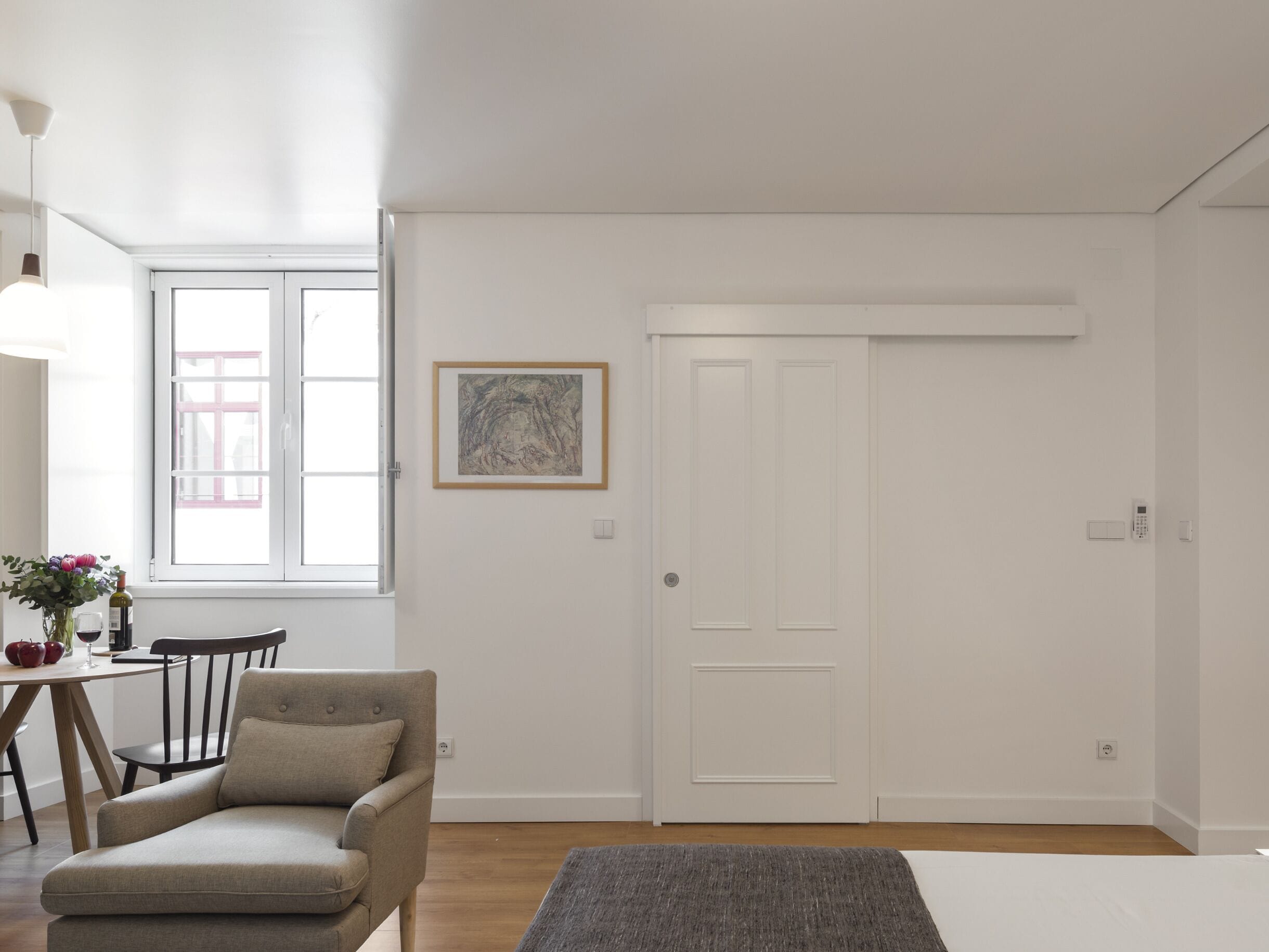 A modern living room with a sofa, a dining table with chairs, a painting on the wall, and a sliding door.