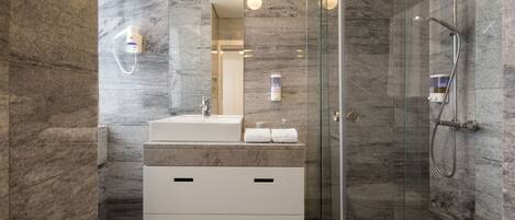 A modern bathroom with a glass-enclosed shower, marble walls, and a white vanity with drawers.