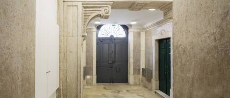 A hallway with a large, dark wooden door, a green door to the right, and a white door at the end.